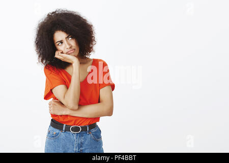 Studio shot of upset girl sentiment de regret et de l'ennui, leaning head sur palm, bouder et regarder l'angle supérieur droit, désireux d'être dans un autre lieu, l'article triste et fatigué sur fond gris Banque D'Images