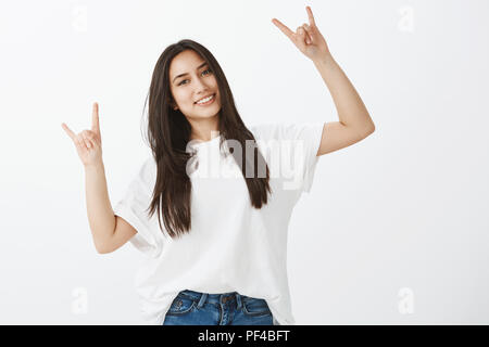 Tourné à l'intérieur de bon à la femelle adulte dans la région de White T-shirt et jeans, élever les mains avec des gestes rock et tout sourire, heureux et grand lors de concerts, smiling at camera 2 étoiles Banque D'Images