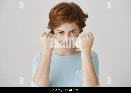 Vous feriez mieux de ne pas jouer avec moi, mon garçon. Emotive rousse mignon femme européenne à la recherche de dessous les sourcils holding poings près de visage et sourire, essayant d'avoir l'air agressif et prêt à la défense Banque D'Images