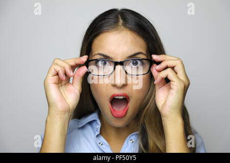 Portrait de jeune femme tenant ses lunettes qui ne croit pas ce qu'elle lookings isolé sur fond gris Banque D'Images