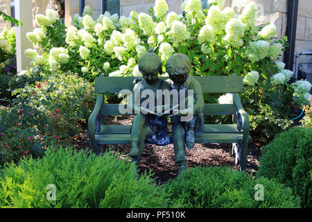 Un vintage statue d'un garçon et une fille assise sur le banc et lire un livre dans le jardin Banque D'Images