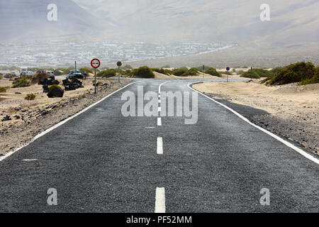 Desert route asphaltée avec un petit village typique de l'île de Lanzarote sur l'arrière-plan, Îles Canaries Banque D'Images