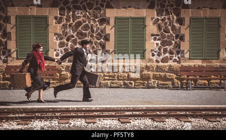 Jeune couple avec vintage suitcase tourne vite à l'extérieur d'une gare pour attraper le dernier train pour le voyage. Banque D'Images