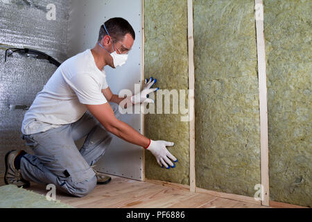 Travailleur dans des lunettes et un masque respiratoire l'isolation isolation laine de roche dans le cadre en bois pour les murs de maison pour barrière froide. Chaud confortable Banque D'Images