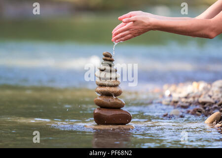 Close-up résumé image de femme part verser de l'eau sur les différentes tailles inégales brun naturel et la forme des pierres comme équilibrée pile pyramide monument Banque D'Images