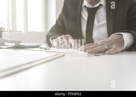 Businessman working on ses comptes dans un angle bas vue sur le bureau de ses mains aux formalités administratives à l'aide d'une calculatrice à côté. Banque D'Images