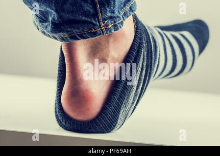 Homme avec une ampoule sur le talon avec son sock levé pour révéler la matière première pastille rouge de décoloration de la peau. Avec un style vintage effet filtre instagram. Banque D'Images