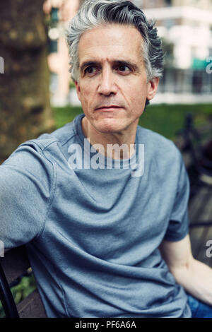 L'homme aux cheveux gris s'assoit sur un banc de parc Banque D'Images