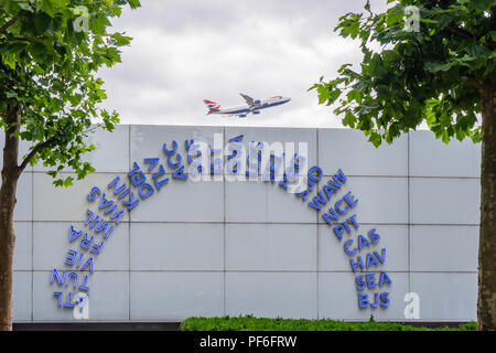 Codes IATA mondiaux bleus illuminés affichés à l'extérieur du terminal 5 de l'aéroport de Londres Heathrow, décollage de l'avion des voies aériennes britanniques en arrière-plan, Royaume-Uni Banque D'Images