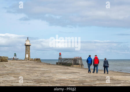 Balades en famille le long de la jetée Est à Whitby, sur la côte de North Yorkshire, Angleterre. Un couple d'âge mûr et son fils se promener vers le phare. Banque D'Images