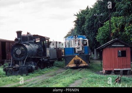 Managua, Nicaragua, 12 février 1990, un train de marchandises par chemin de fer gare de disques dans Managua, passé sur la vieille machine à vapeur abandonnés stationné dans un garage. Banque D'Images