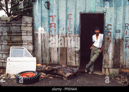 Managua, Nicaragua, juillet 1986 ; un jeune garçon roule une roue qui a été réparée par l'atelier de mécanique derrière. Banque D'Images