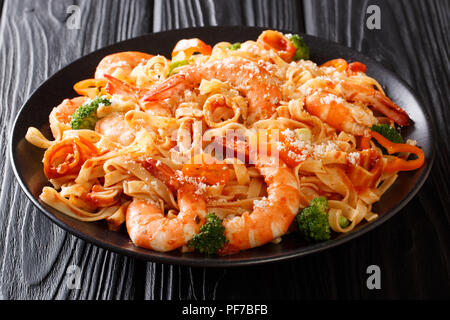 La cuisine italienne : pâtes aux calamars, crevettes tiger, légumes, fromage parmesan et sauce tomate close-up sur une plaque sur une table. Délicieux dîner Banque D'Images