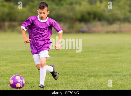 Boy kicking football sur le terrain de sport au cours de match de football Banque D'Images