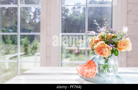 Magnifique bouquet de roses de l'été Anglais orange vase en verre bocal, près de la grande fenêtre en bois blanc sur la table Banque D'Images