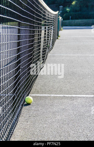Low angle view of d'une balle de tennis jaune sur le sol près du filet d'une surface dure de tennis Banque D'Images