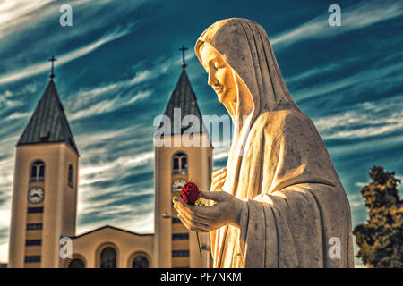 Statue de la Vierge Marie tenant une rose rouge alors que l'église Saint Jacques de Medjugorje est en arrière-plan Banque D'Images