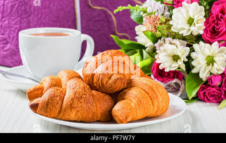 Croissants français sur le plat blanc, tasse de thé et de bouquet de fleurs fraîches sur d'anciennes planches de bois, belle fort enveloppée de papier et décoré de ribbo Banque D'Images