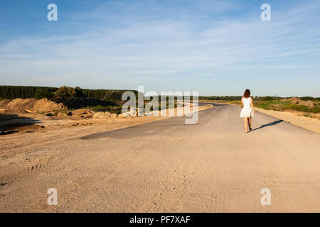 Déçu femme debout au milieu de la construction routière et de la tenue d'un tournesol cassé pendant le coucher du soleil. La destruction de l'environnement concept. Banque D'Images