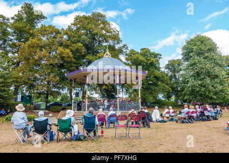 Un groupe joue un concert gratuit dans la région de band stand Alexandra Gardens à Windsor, Royaume-Uni. Les gens s'assoient sur des chaises pliantes, benchses et le sol à regarder. Banque D'Images