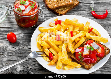 Pomme de terre frites avec des morceaux de piment sur le plat blanc et tranches de hareng norvégien mariné dans de la sauce tomate sur les morceaux de pain de seigle, le g Banque D'Images