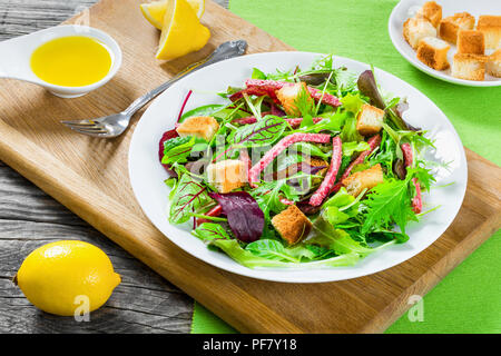 Délicieuse salade fraîche de salami et mixte - feuilles de laitue roquette, jeunes épinards, blettes dans un plat blanc sur la vieille table en bois, vue du dessus Banque D'Images