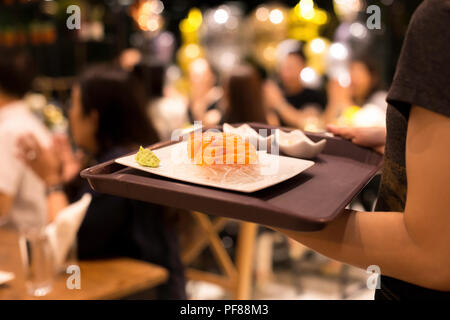 Franc tourné en haute iso avec faible lumière waitress serving salmon sashimi à client en restaurant Banque D'Images