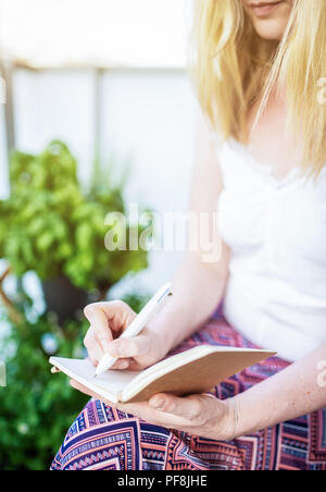 Femme assise sur le patio en prenant des notes dans l'ordinateur portable Banque D'Images