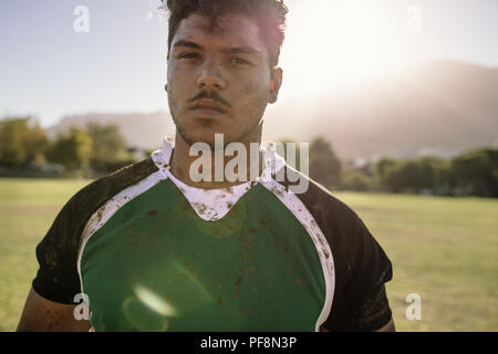 joueur de rugby sur le terrain de sport. Jeune sportif avec le visage et uniforme enduit dans la boue avec la lumière du soleil brillant. Banque D'Images