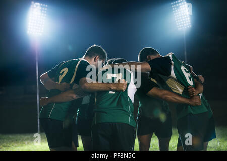joueurs de rugby debout ensemble après le match sous les lumières. équipe de rugby en caucus dans l'arène sportive la nuit. Banque D'Images