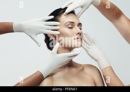 Deux esthéticiennes et toucher la peau du visage de l'examen d'une femme. Woman face à contrôler les esthéticiennes mains en studio. Banque D'Images