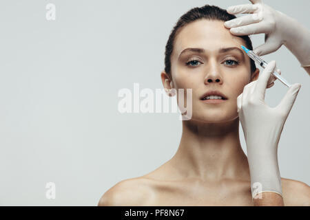 Femme d'injection sur le front. Chirurgie esthétique anti rides au niveau du front fait par médecin esthétique sur fond gris. Banque D'Images