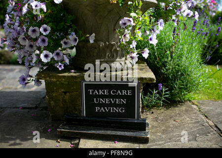 Libre de prendre soin de pavage inégal signe de sécurité dans un jardin de campagne anglaise uk Banque D'Images