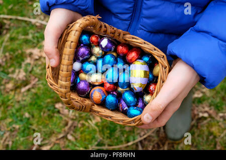 Gros plan des œufs de Pâques au chocolat enveloppés dans du papier d'aluminium coloré de divers magasins dans le panier ramassé par enfant sur un Chasse aux œufs de Pâques, Royaume-Uni KATHY DEWITT Banque D'Images