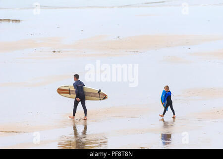 Un père et son fils marchant sur la plage de Fistral transportant un surf et un corps boogie board sur un coild journée d'été. Banque D'Images