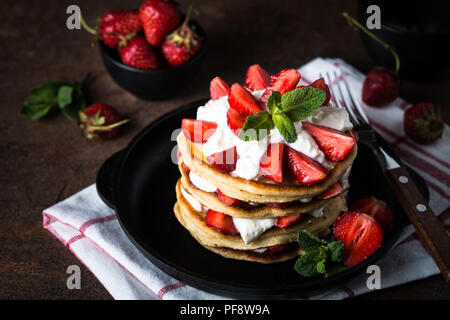 Gâteau de crêpes à la crème fouettée et les fraises. Fond rustique foncé. Banque D'Images