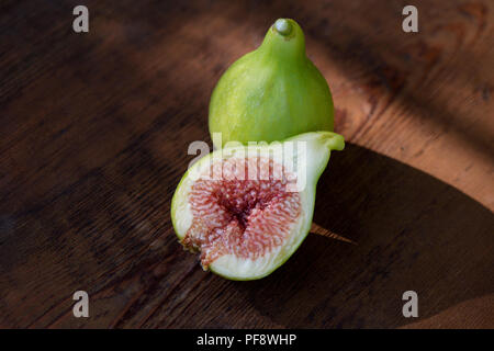 Bio, mûres fraîchement cueillies figues Kadota sur une table, un fruit coupé en deux, la pâte mauve montrant toujours des aliments sur la vie artistique de fond en bois Banque D'Images