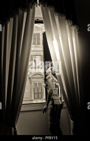 Jeune femme ouvre les rideaux et regarde par la fenêtre sur un matin ensoleillé dans une grande ville Banque D'Images