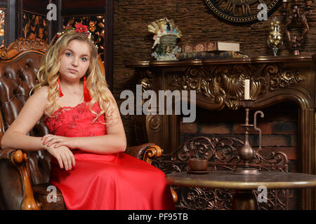 Adolescente blonde en robe rouge vif sitting in armchair Banque D'Images