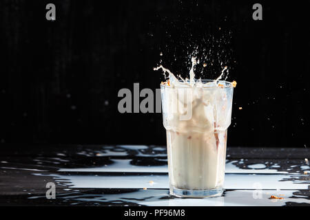 Éclaboussures de lait de la vitre à l'Oat muesli et lait renversé sur une table en bois noir avec place pour le texte. Banque D'Images