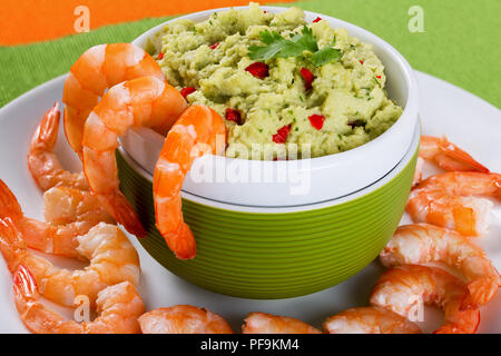 Queues de crevettes géantes cuites sur une plaque blanche avec guacamole sauce dans un bol vert sur un tapis de table sur une vieille table rustique, projecteurs, close-up Banque D'Images