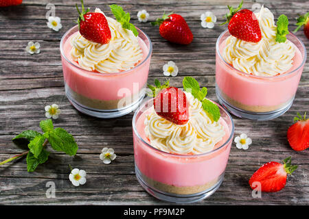 Gâteau au fromage aux fraises Mousse tasses décorées par les glaces maison, les feuilles de menthe et de fleurs de fraises sur une vieille table en bois rustique, studio lumineux, à Banque D'Images