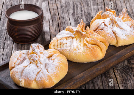 Feuilletés de noix de coco avec du sucre en poudre poussière sur une carte mère sur un vieux fond de bois avec du lait dans une tasse, rustique d'argile vue du dessus, à proximité- Banque D'Images