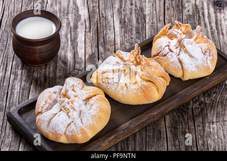 Feuilletés de noix de coco avec du sucre en poudre poussière sur une carte mère sur un vieux fond de bois avec du lait dans une tasse, rustique d'argile vue du dessus, à proximité- Banque D'Images