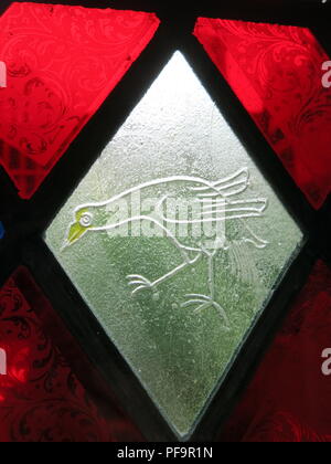 Vue rapprochée d'un oiseau représenté dans un vitrail, entouré par des panneaux de verre rouge ; Baddesley Clinton (National Trust), Warwickshire. Banque D'Images