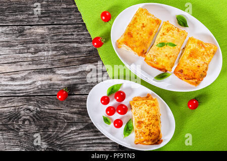 Crêpes roulées ou des crêpes farcies de viande hachée et de légumes sur des plats ovales avec les tomates cerises et le basilic, la vue de dessus Banque D'Images