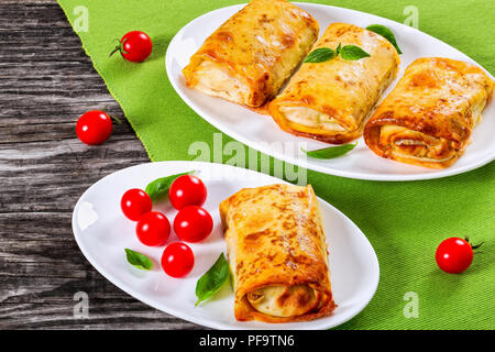 Crêpes roulées ou des crêpes farcies de viande hachée et de légumes sur des plats ovales avec les tomates cerises et le basilic, la vue de dessus Banque D'Images