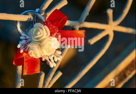 Blocage de mariage avec des roses blanches et ruban rouge sur le pont métallique qui brille sous la lumière du soleil Banque D'Images