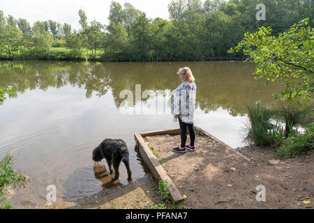 Blonde mature dame se trouve aux côtés du lac à trois soeurs la réserve naturelle locale, trois Sœurs Road, Ashton-In-Makerfield, Wigan avec son black Banque D'Images