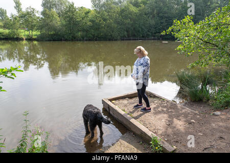 Blonde mature dame se trouve aux côtés du lac à trois soeurs la réserve naturelle locale, trois Sœurs Road, Ashton-In-Makerfield, Wigan avec son black Banque D'Images